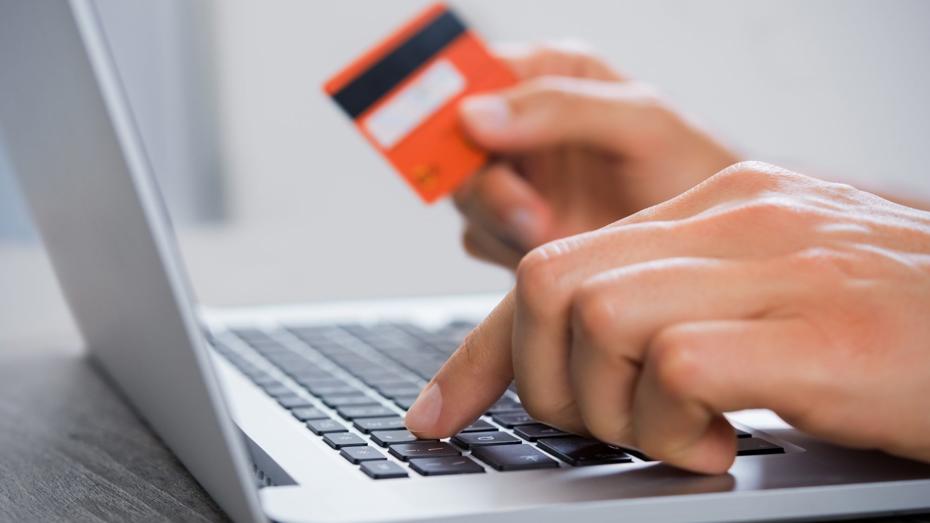 Hands using a laptop keyboard while holding an orange credit card, indicating an online payment or purchase. Hands using a laptop keyboard while holding an orange credit card, indicating an online payment or purchase.