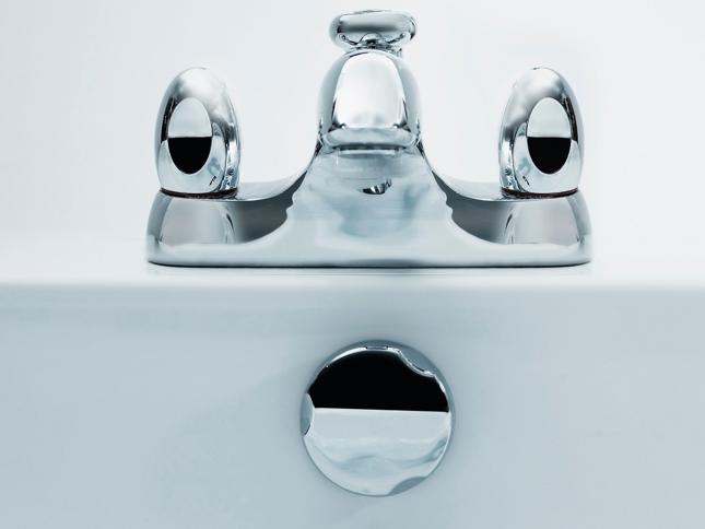 Close-up of a modern chrome bathroom faucet with two handles and a central spout, mounted on a white sink. Close-up of a modern chrome bathroom faucet with two handles and a central spout, mounted on a white sink.