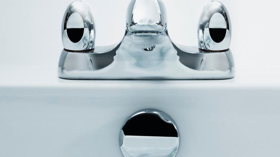Close-up of a modern chrome bathroom faucet with two handles and a central spout, mounted on a white sink. Close-up of a modern chrome bathroom faucet with two handles and a central spout, mounted on a white sink.