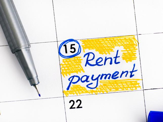 A close-up of a calendar page with the date 15 circled in blue and the words “Rent payment” written in blue ink on a yellow highlighted background. A pen is visible near the top left. A close-up of a calendar page with the date 15 circled in blue and the words “Rent payment” written in blue ink on a yellow highlighted background. A pen is visible near the top left.