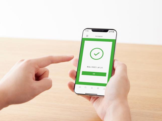 A person holding a smartphone displaying a payment confirmation screen with a green checkmark and Japanese text, along with an “OK” button. A person holding a smartphone displaying a payment confirmation screen with a green checkmark and Japanese text, along with an “OK” button.