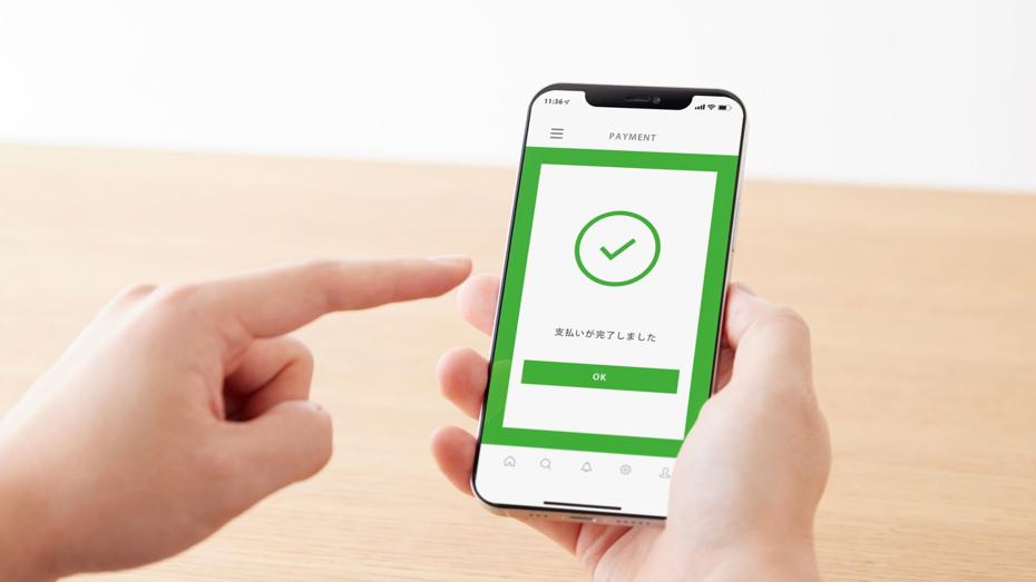 A person holding a smartphone displaying a payment confirmation screen with a green checkmark and Japanese text, along with an “OK” button. A person holding a smartphone displaying a payment confirmation screen with a green checkmark and Japanese text, along with an “OK” button.