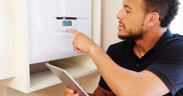 Person pointing at the control panel of a white appliance, possibly a boiler, while holding a tablet.