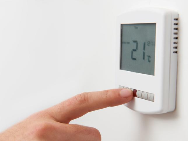 Close-up of a hand adjusting a digital thermostat displaying a temperature of 21°C. Close-up of a hand adjusting a digital thermostat displaying a temperature of 21°C.