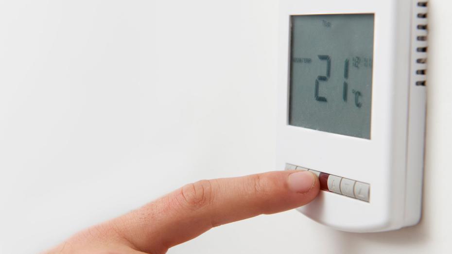 Close-up of a hand adjusting a digital thermostat displaying a temperature of 21°C. Close-up of a hand adjusting a digital thermostat displaying a temperature of 21°C.