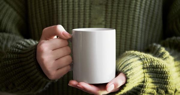 Hands holding a plain white mug, with the person wearing a green knitted sweater, evoking warmth and comfort.