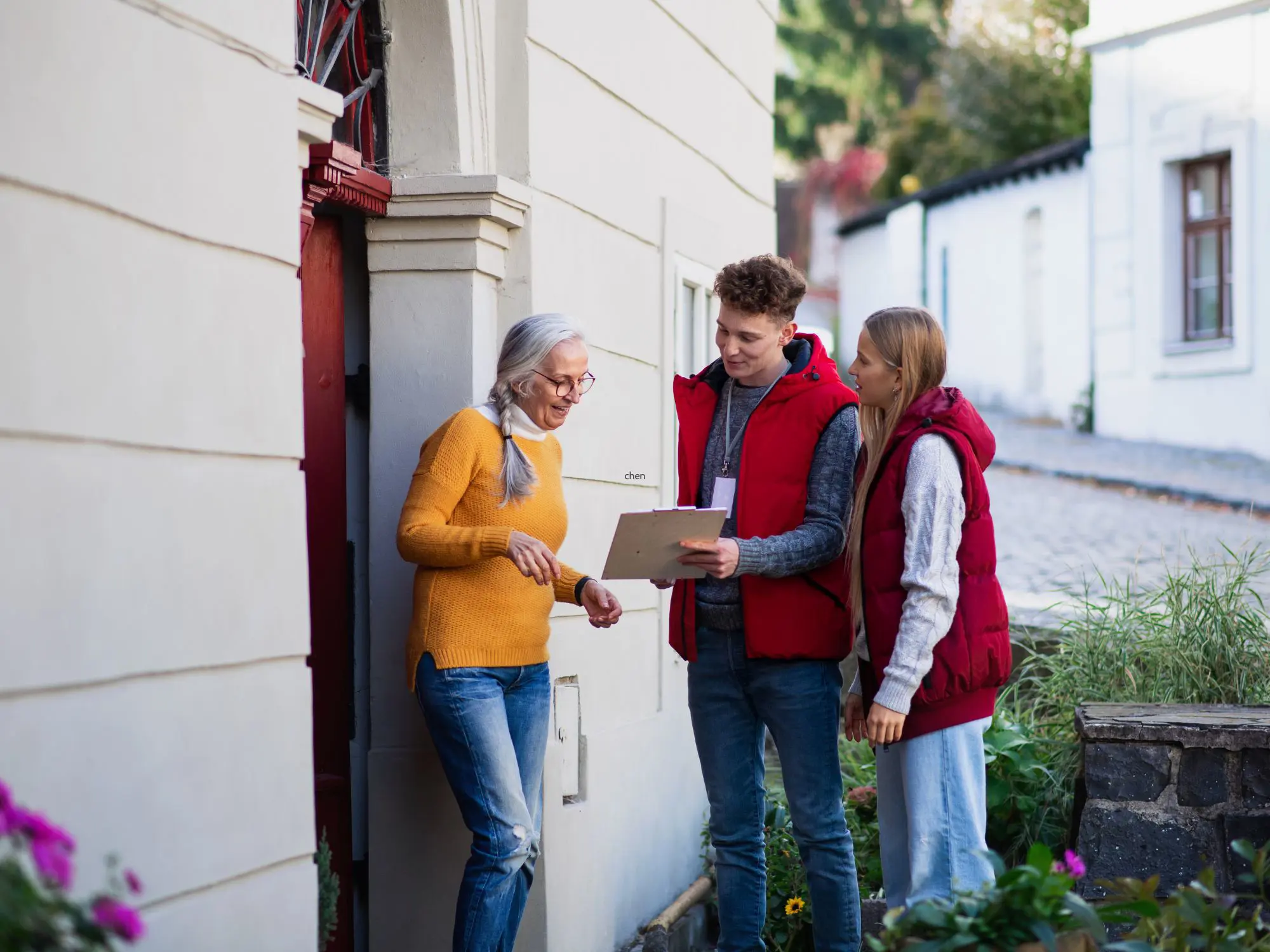Three people standing outside in a residential area, with one person holding a clipboard and engaging in discussion with the others.