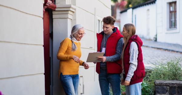 Three people standing outside in a residential area, with one person holding a clipboard and engaging in discussion with the others.