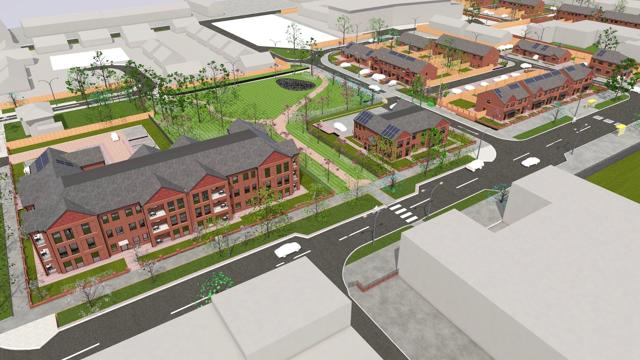 Aerial view of a planned residential development featuring red brick multi-story buildings, smaller homes with solar panels, organized streets, crosswalks, sidewalks, and landscaped green spaces with trees and grass.