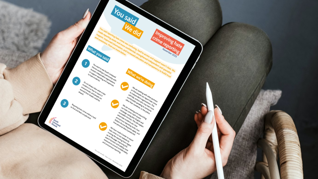 Person sitting with a tablet, holding a stylus pen, viewing a “You said, we did” update titled “Improving hate crime reporting” with sections outlining feedback and actions taken.