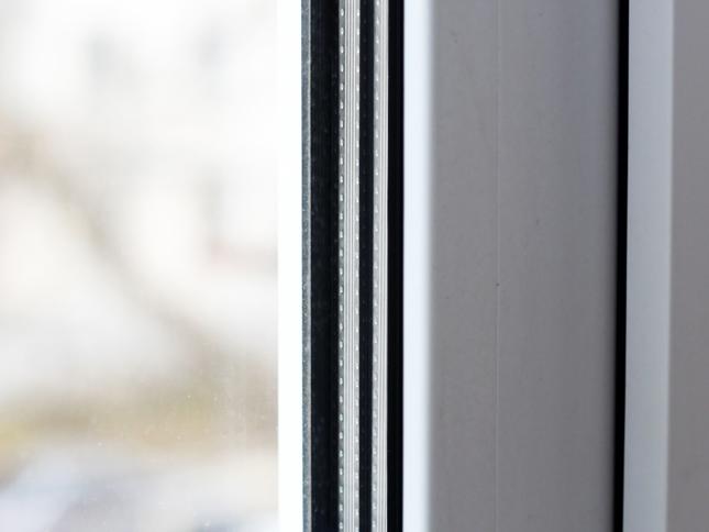 Close-up of a double-glazed window frame showing the seal and spacer between two glass panes, with a blurred outdoor background. Close-up of a double-glazed window frame showing the seal and spacer between two glass panes, with a blurred outdoor background.
