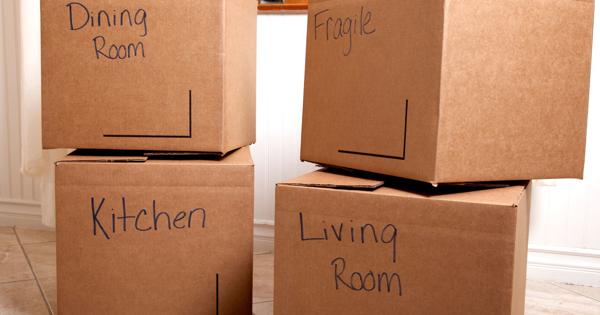 Four labeled cardboard boxes stacked in a room, with handwritten markings reading 'Dining Room', 'Fragile', 'Kitchen', and 'Living Room'—representing a household move or packing process.