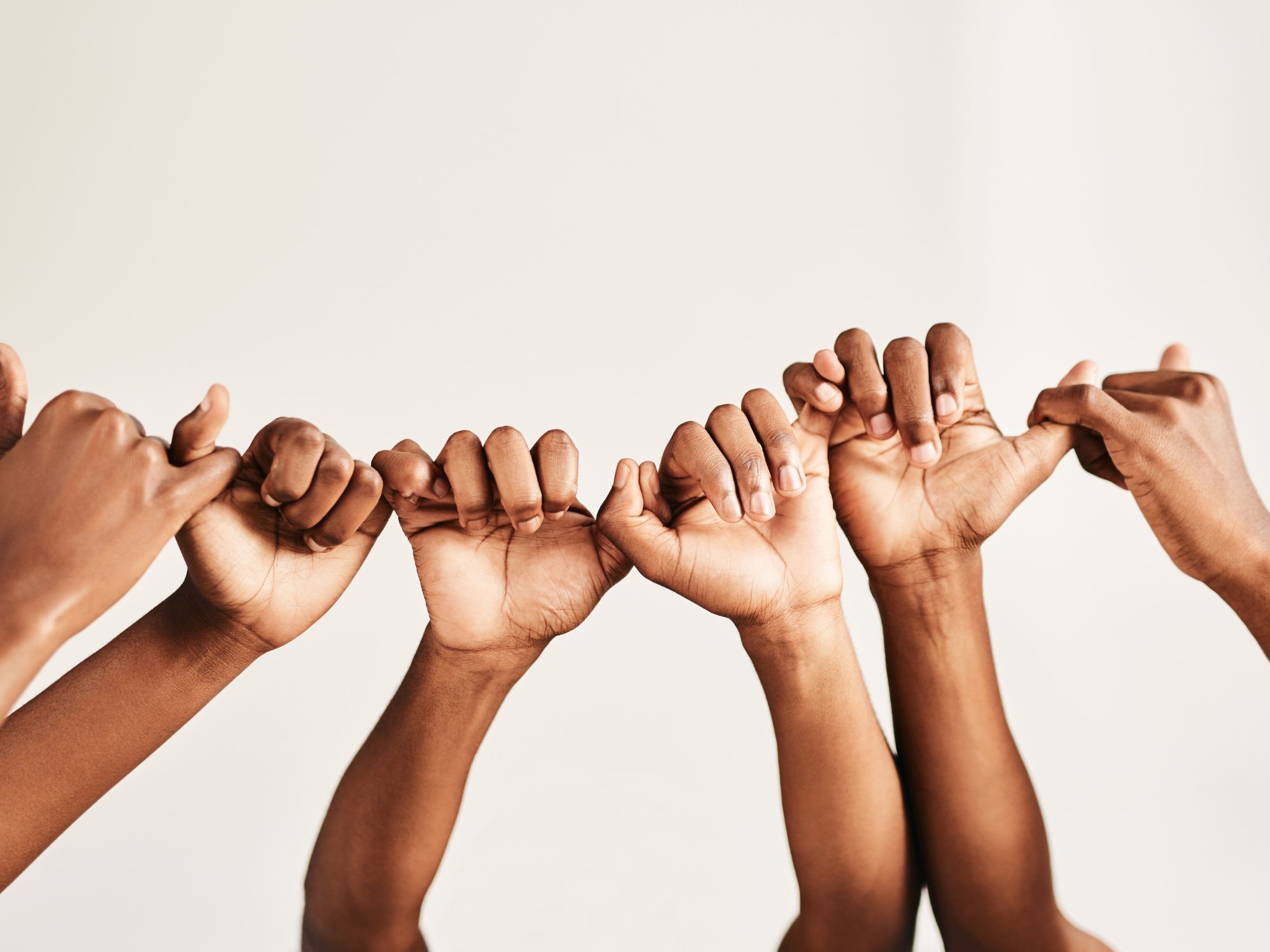 Group of hands linking pinkie fingers in unity, symbolising trust, connection, and access to community safety resources and support.