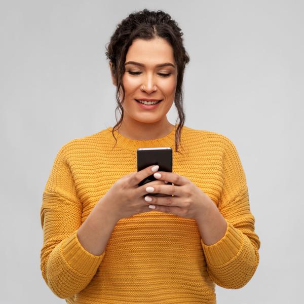 Person in a mustard yellow sweater holding and looking at a smartphone, with a plain light gray background and blurred face.