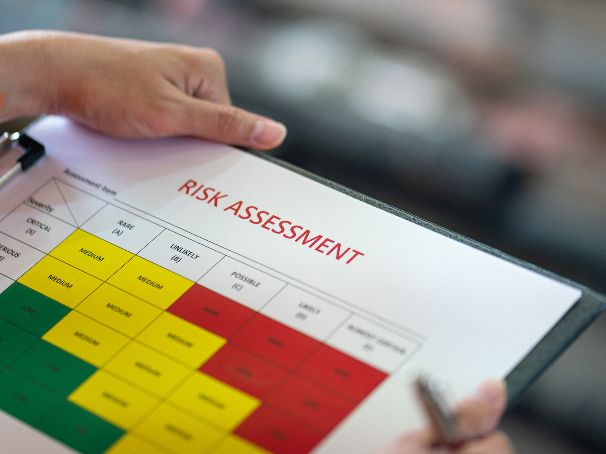 A person holding a clipboard displaying a color-coded risk assessment chart with likelihood levels from "Rare (A)" to "Almost Certain (E)" and impact levels from "Insignificant" to "Critical".