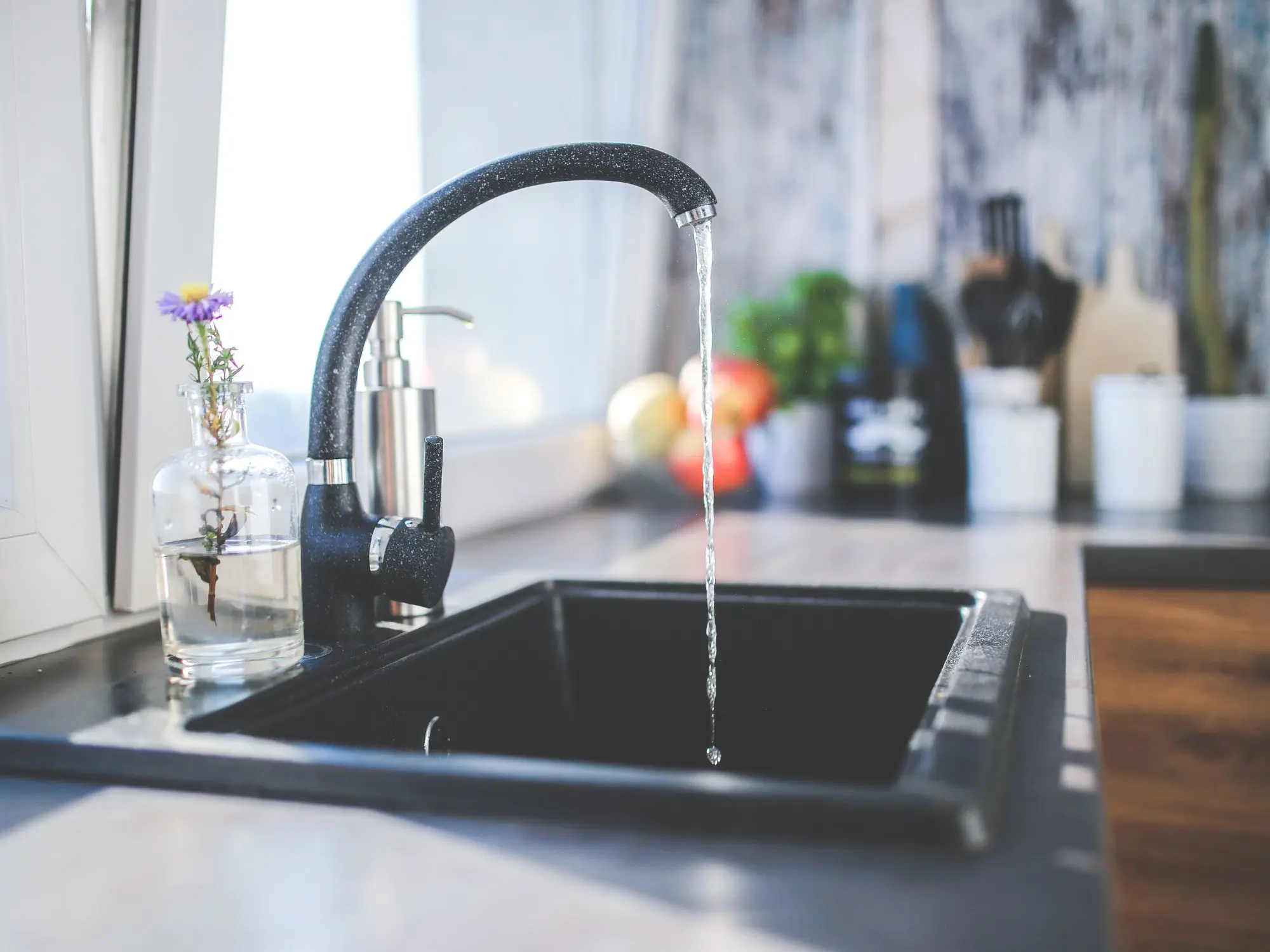 Water running from a kitchen tap into the sink with utensils nearby.
