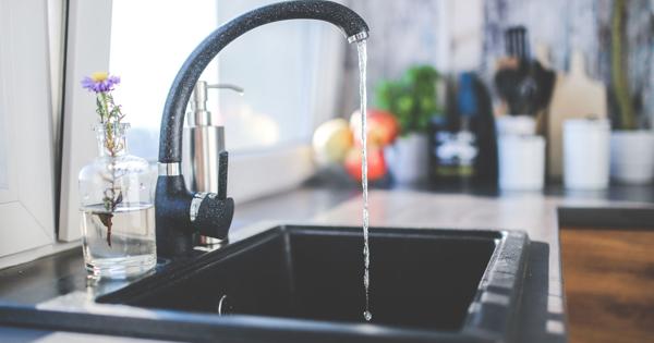 Water running from a kitchen tap into the sink with utensils nearby.