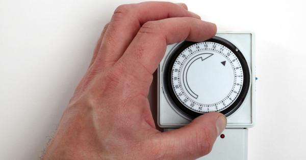 A hand adjusting a circular mechanical timer switch with numbered time intervals around the dial, used for setting on/off times for electrical devices.