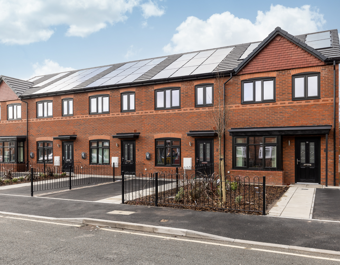 A row of red-brick, new-build homes with driveways in the foreground and a blue sky with white clouds in the background.