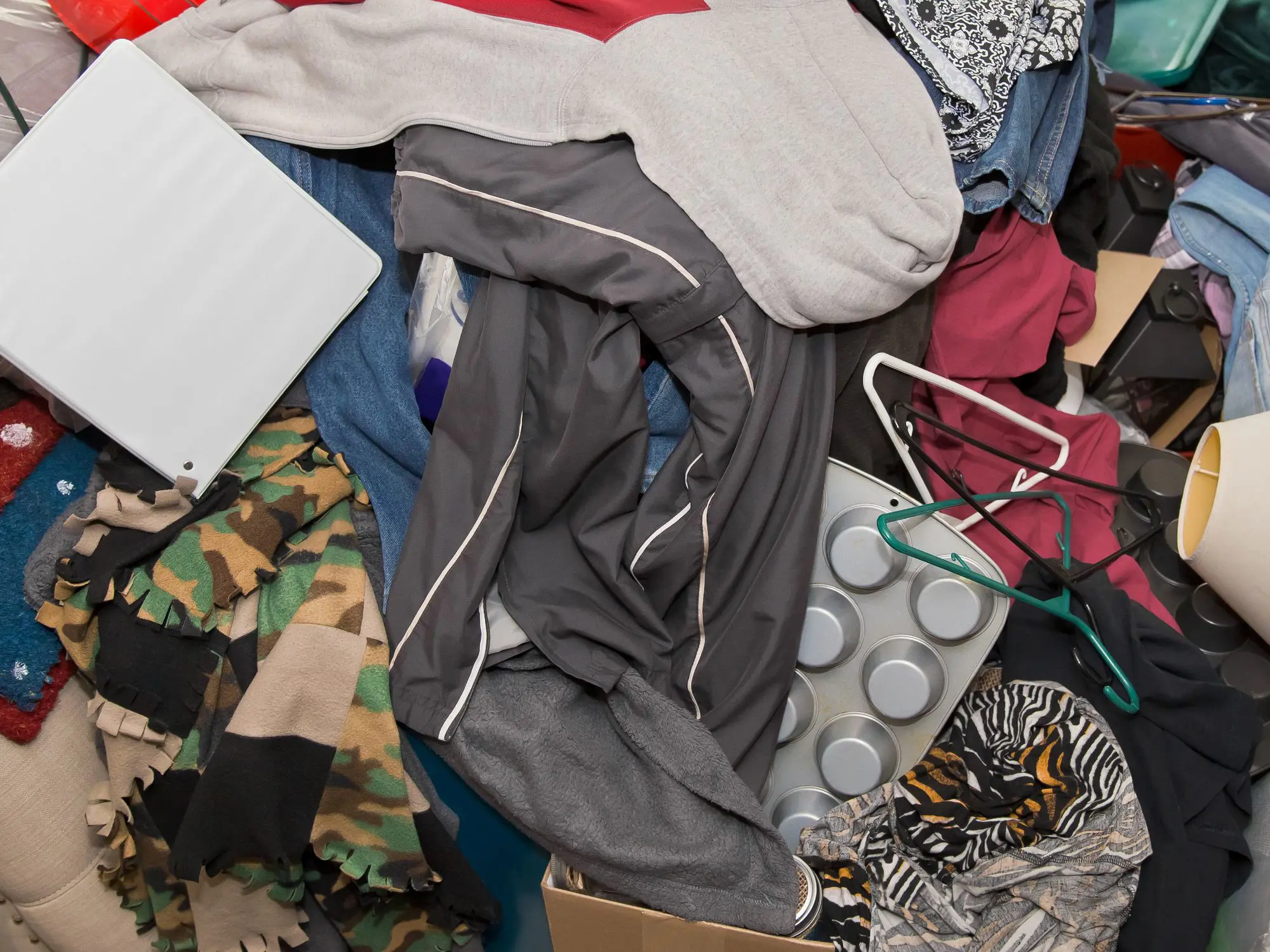A cluttered pile of assorted items including clothes, hangers, and an electronic device, possibly a tablet.