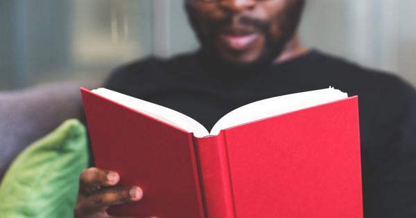 Person reading a bright red book indoors at The Market Place Social, with green cushions visible in the background.