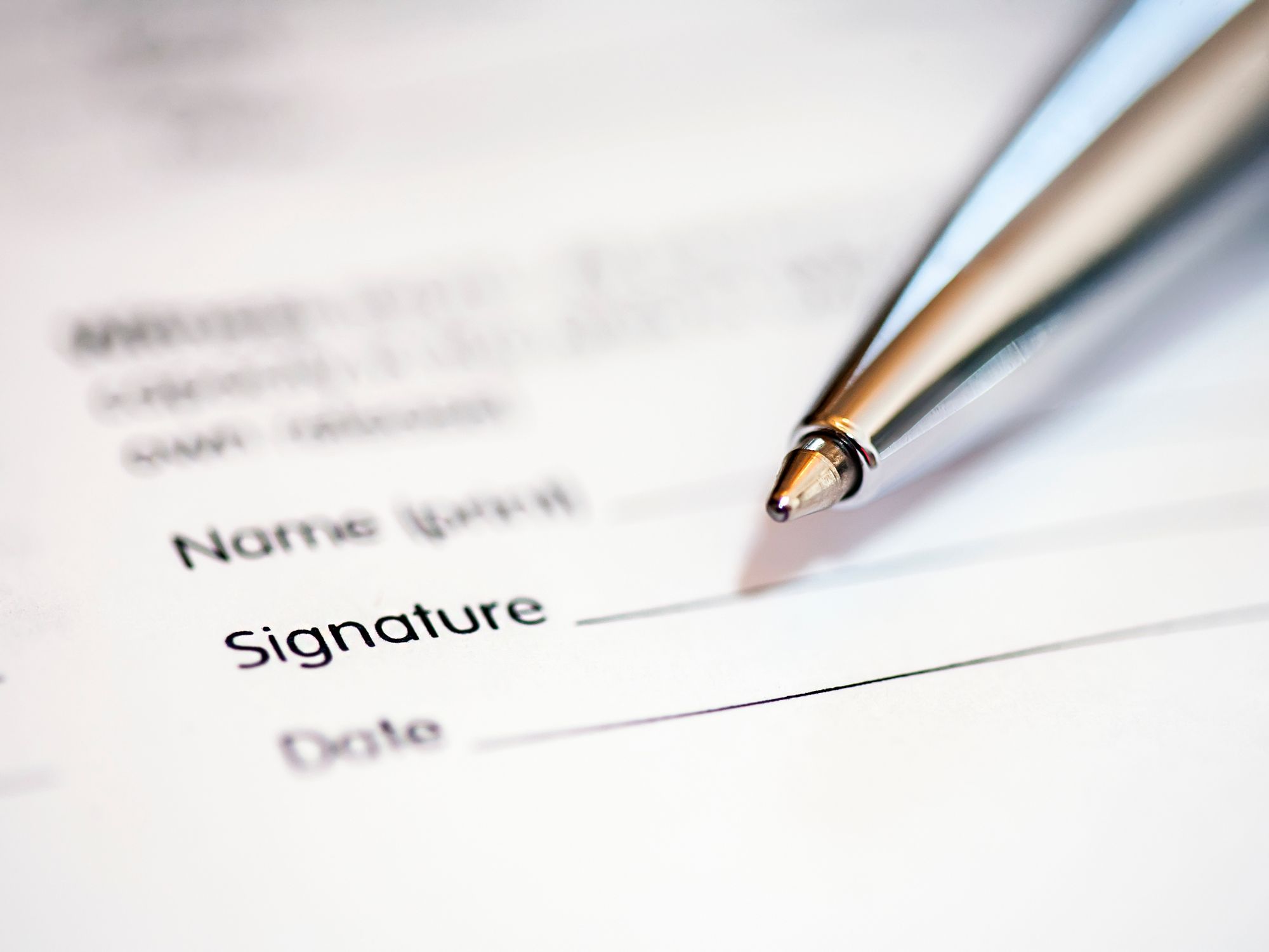 Close-up of a pen resting on a document with fields for name, signature, and date—representing the process of signing formal paperwork.
