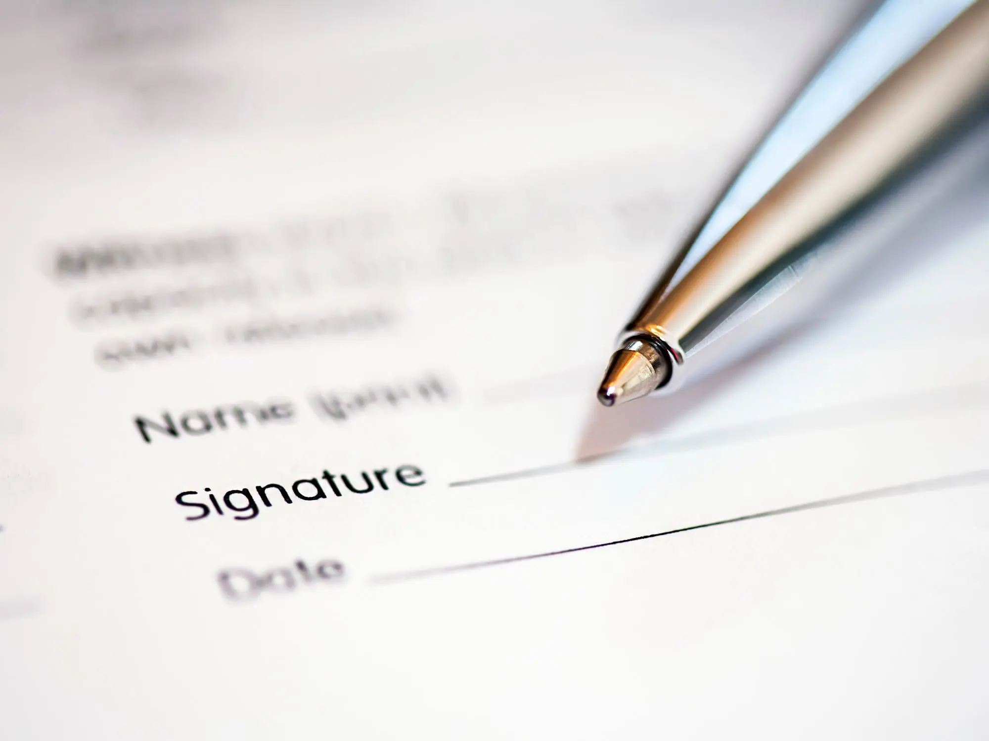 Close-up of a pen resting on a document with fields for name, signature, and date—representing the process of signing formal paperwork.