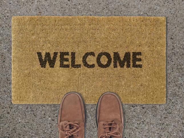 Brown doormat with the word 'WELCOME' in black letters, placed on a concrete surface with two brown shoes visible in front of it. Brown doormat with the word 'WELCOME' in black letters, placed on a concrete surface with two brown shoes visible in front of it.