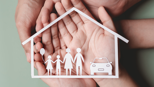 Hands gently holding a paper cut-out of a house containing simple figures of a family and a car, symbolising protection, support and home.