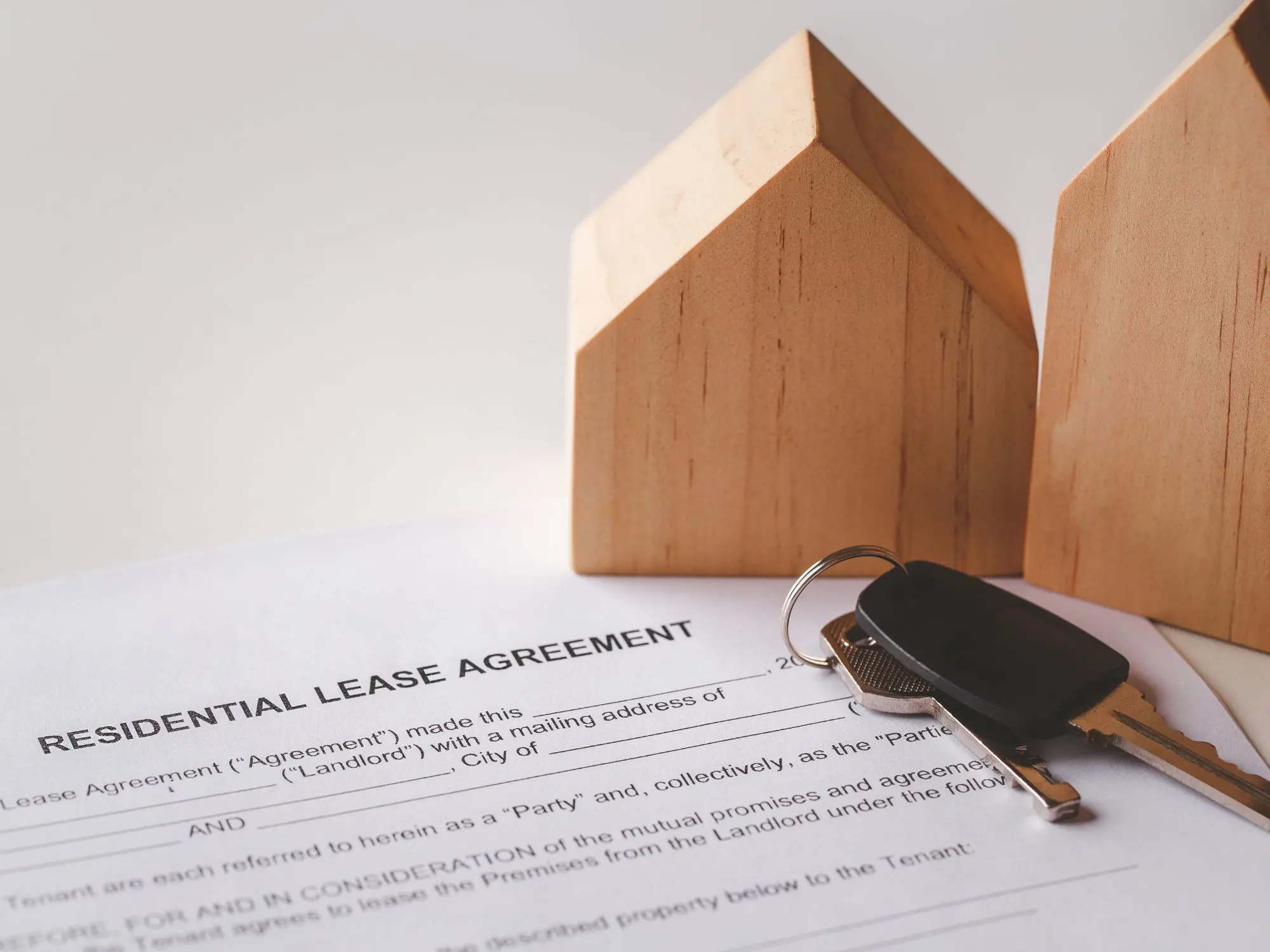 A residential lease agreement document with two wooden house models and a set of keys placed on top—symbolizing property rental and the legal aspects of tenancy.