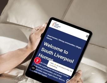 Person holding a tablet displaying the South Liverpool Homes website homepage, which features the text ‘Welcome to South Liverpool Homes’ along with a navigation menu and a live chat pop-up.”