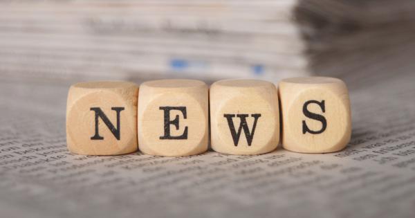 Four wooden blocks spelling “NEWS” placed on top of a newspaper, with a stack of newspapers in the background.
