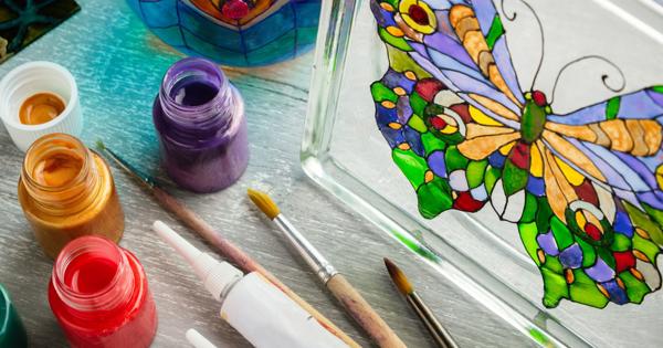 Art supplies and painted glass objects at The Market Place Social, including paintbrushes, open jars of red and purple paint, and glass pieces decorated with butterfly and peacock feather designs.