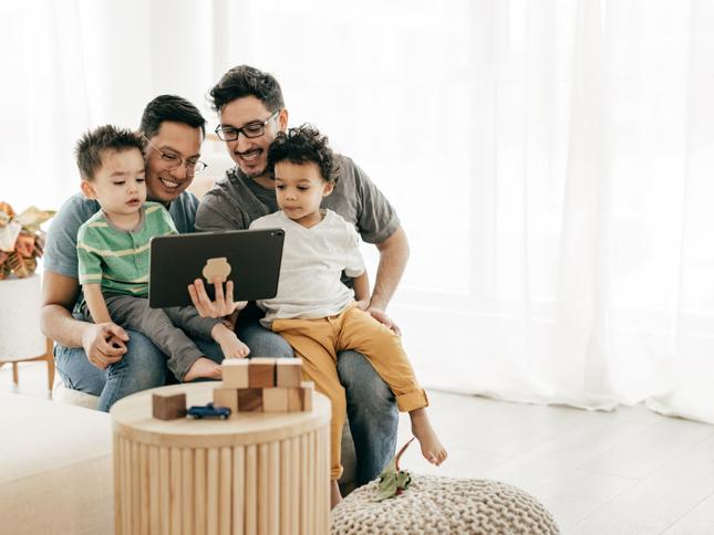 Four people sitting together on a couch, looking at a tablet with toys on the table in front, illustrating family engagement and planning for a future home. Four people sitting together on a couch, looking at a tablet with toys on the table in front, illustrating family engagement and planning for a future home.