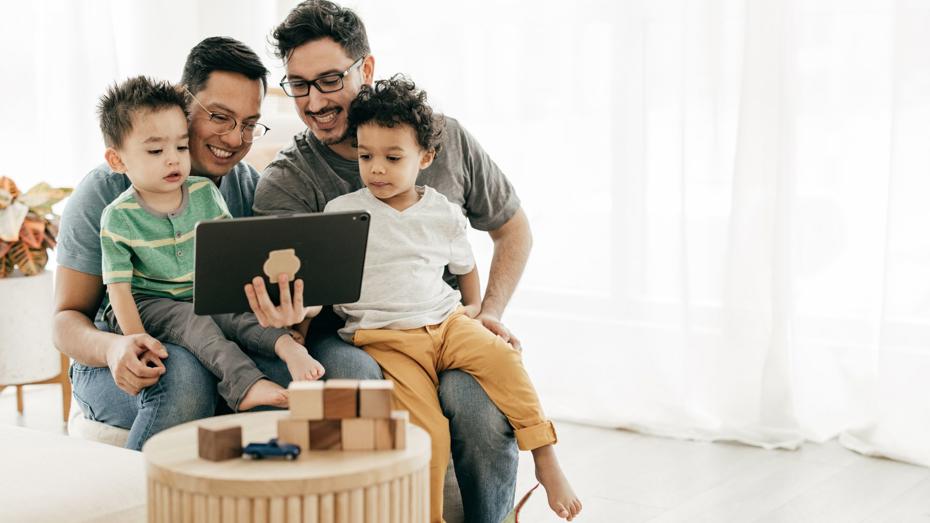 Four people sitting together on a couch, looking at a tablet with toys on the table in front, illustrating family engagement and planning for a future home. Four people sitting together on a couch, looking at a tablet with toys on the table in front, illustrating family engagement and planning for a future home.