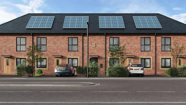 Row of modern apartments with rooftop solar panels, three cars parked in front, and a street with double yellow lines under a partly cloudy sky.