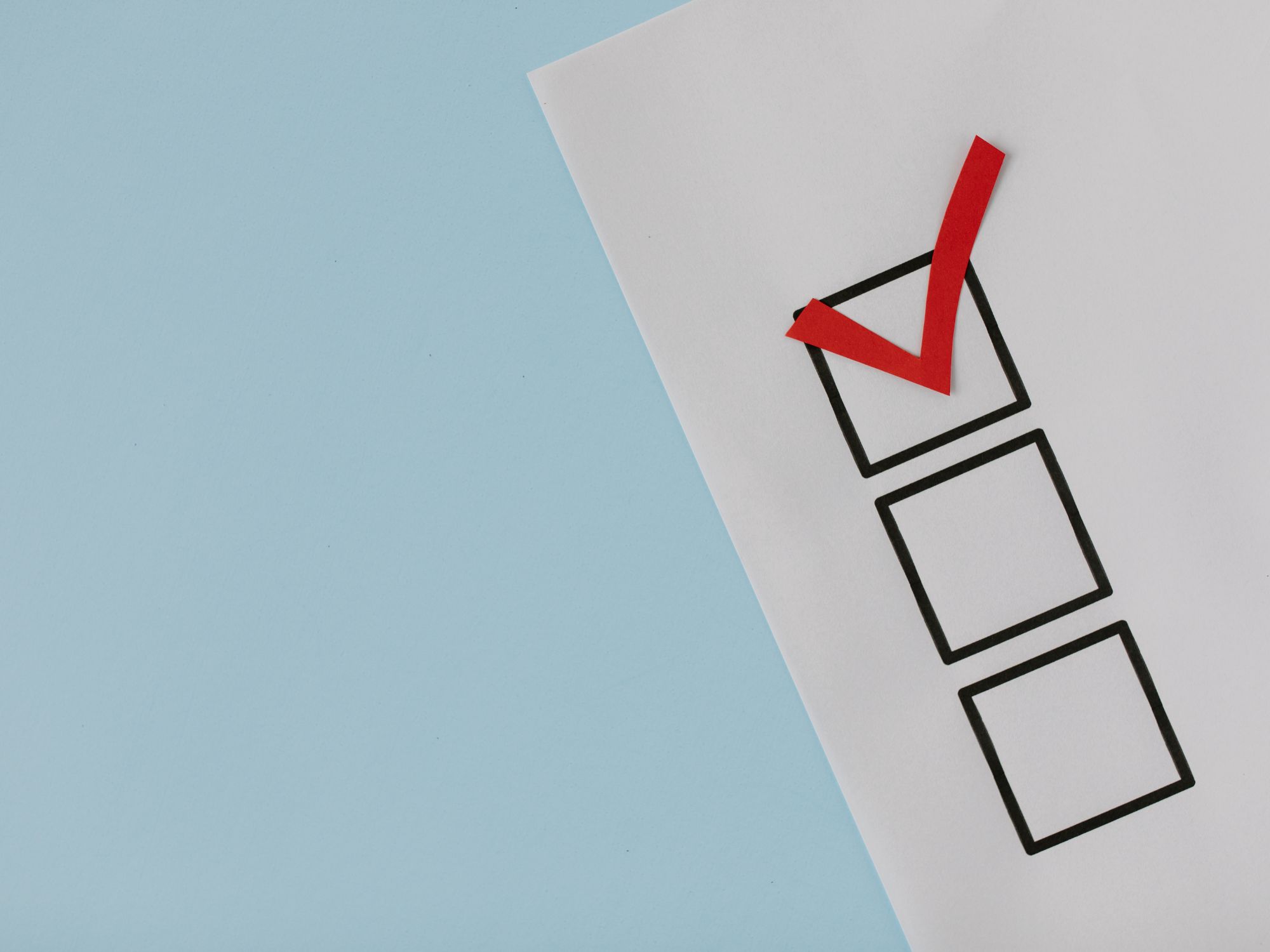 A piece of paper with three vertically arranged checkboxes on a light blue background; the top checkbox is marked with a red checkmark, while the other two are empty.