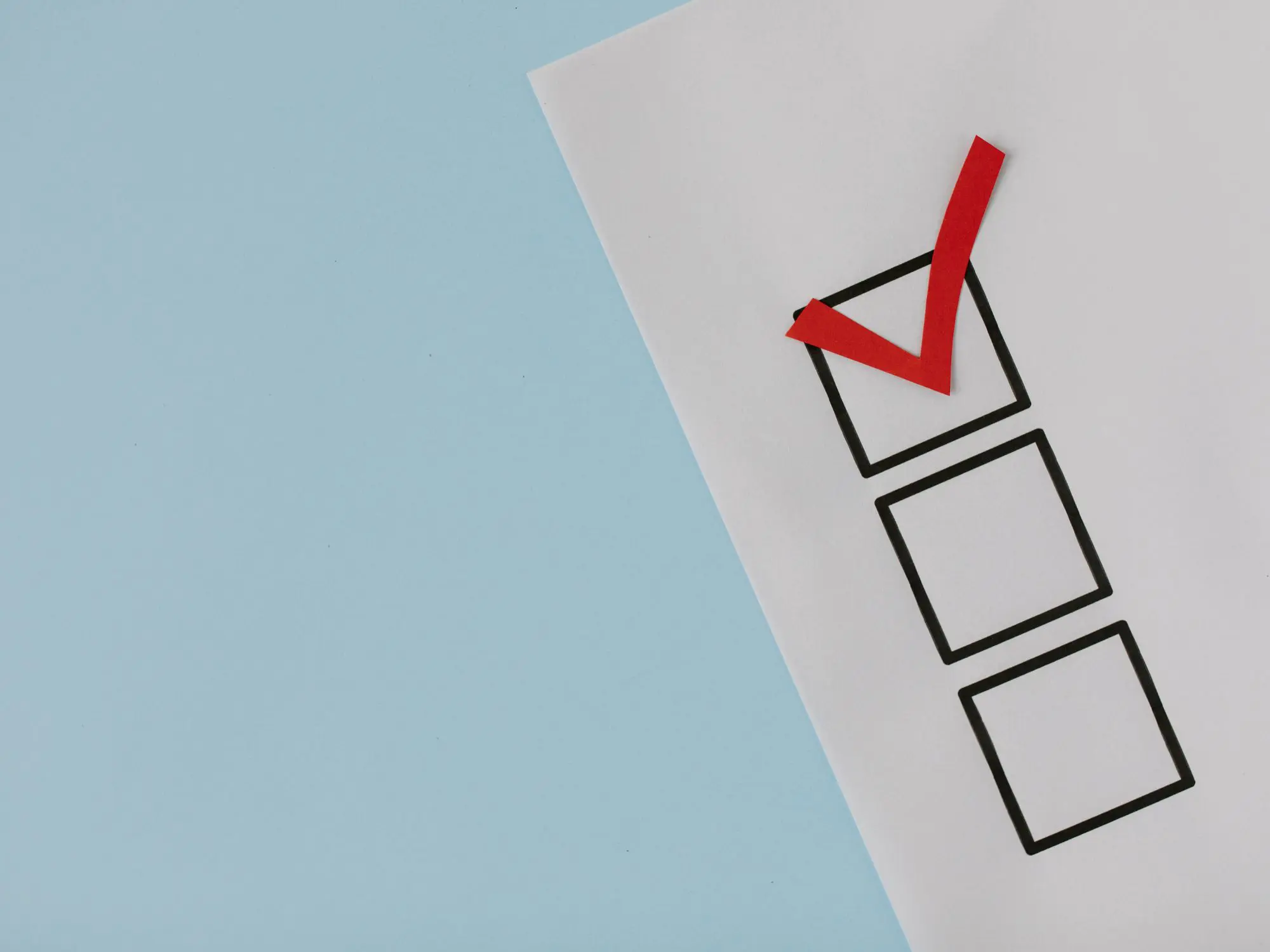 A piece of paper with three vertically arranged checkboxes on a light blue background; the top checkbox is marked with a red checkmark, while the other two are empty.