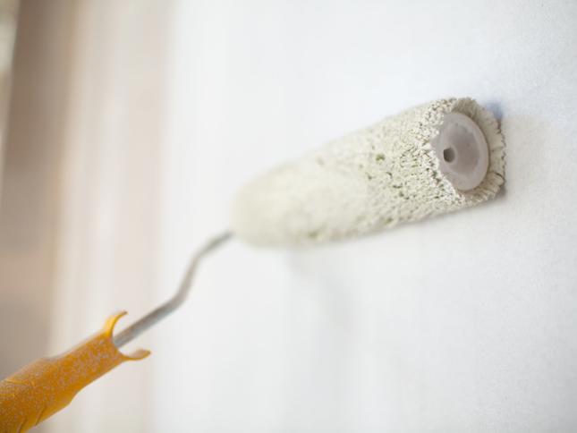 Close-up of a paint roller with an orange handle applying white paint to a wall. Close-up of a paint roller with an orange handle applying white paint to a wall.