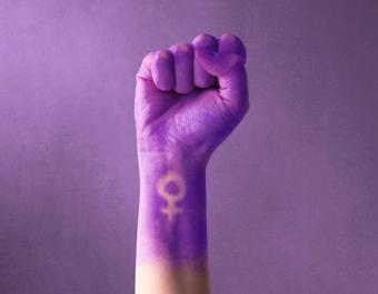 Purple raised fist with Venus symbol on wrist, symbolizing empowerment and solidarity for International Women’s Day.