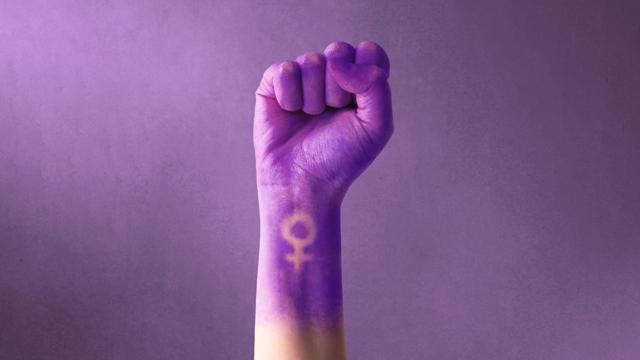 Purple raised fist with Venus symbol on wrist, symbolizing empowerment and solidarity for International Women’s Day.