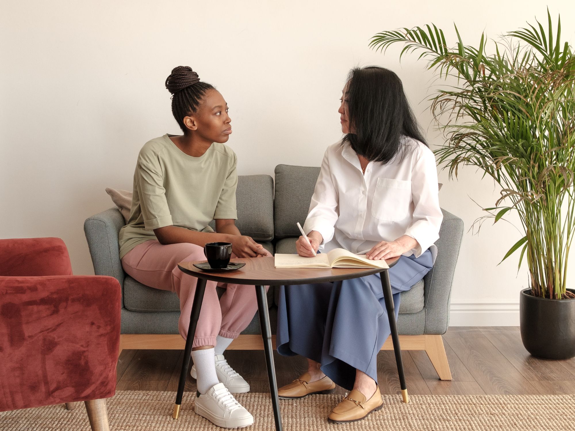 Two people seated on a couch in conversation, with one writing in a notebook, symbolising support and dialogue for witnesses and perpetrators of anti-social behaviour.