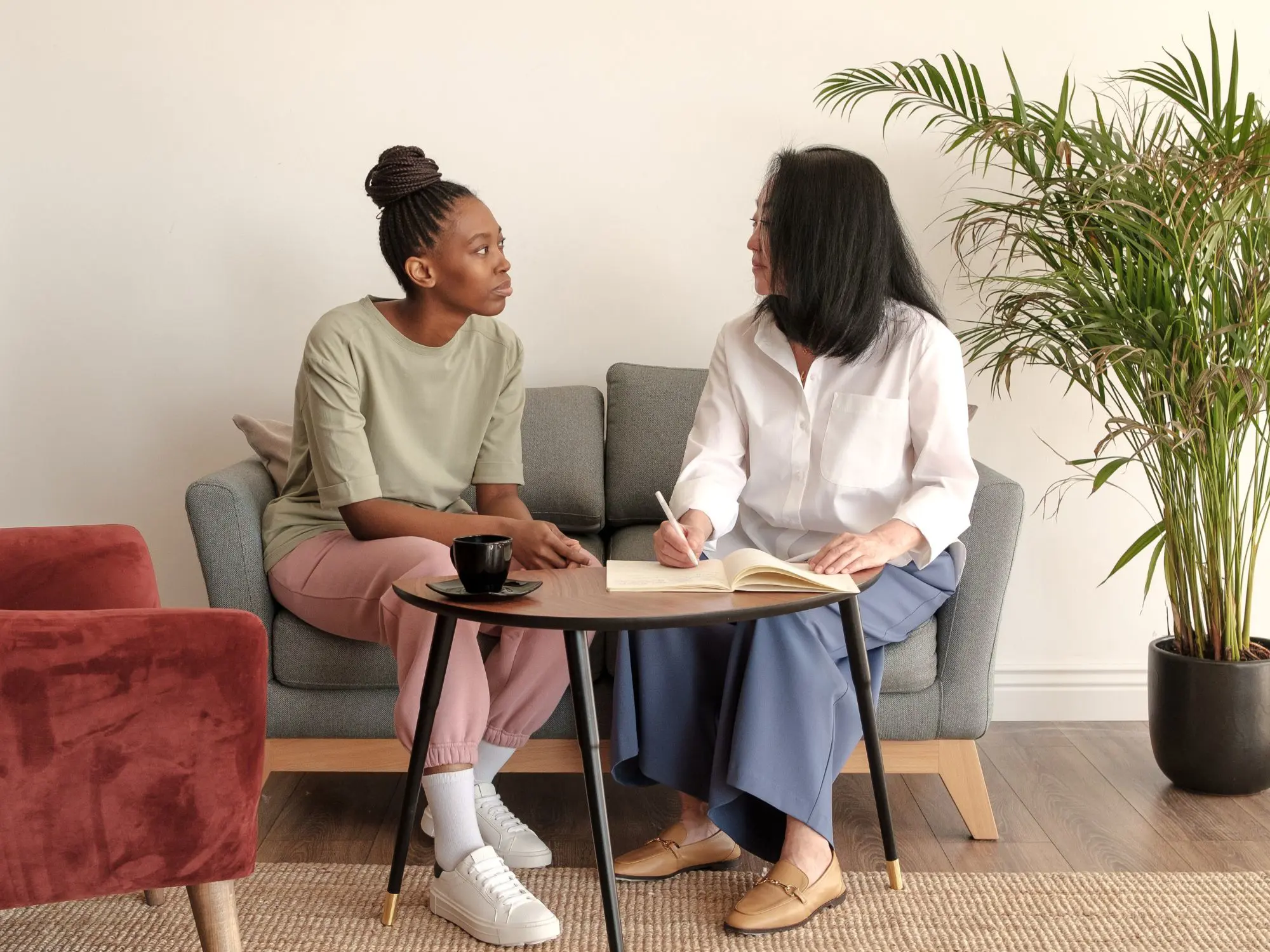 Two people seated on a couch in conversation, with one writing in a notebook, symbolising support and dialogue for witnesses and perpetrators of anti-social behaviour.