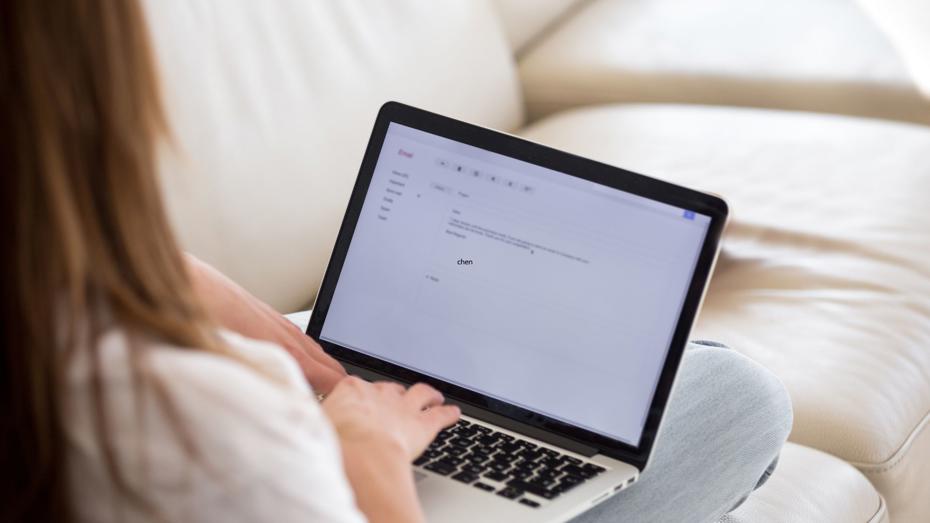 A person sitting on a couch using a laptop, composing an email with the word "chan" visible on the screen. A person sitting on a couch using a laptop, composing an email with the word "chan" visible on the screen.