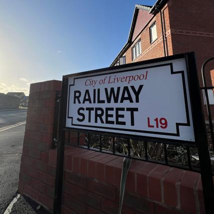 Image of road sign saying 'Railway St' with new build red brick homes in the background, against a clear blue sky. 