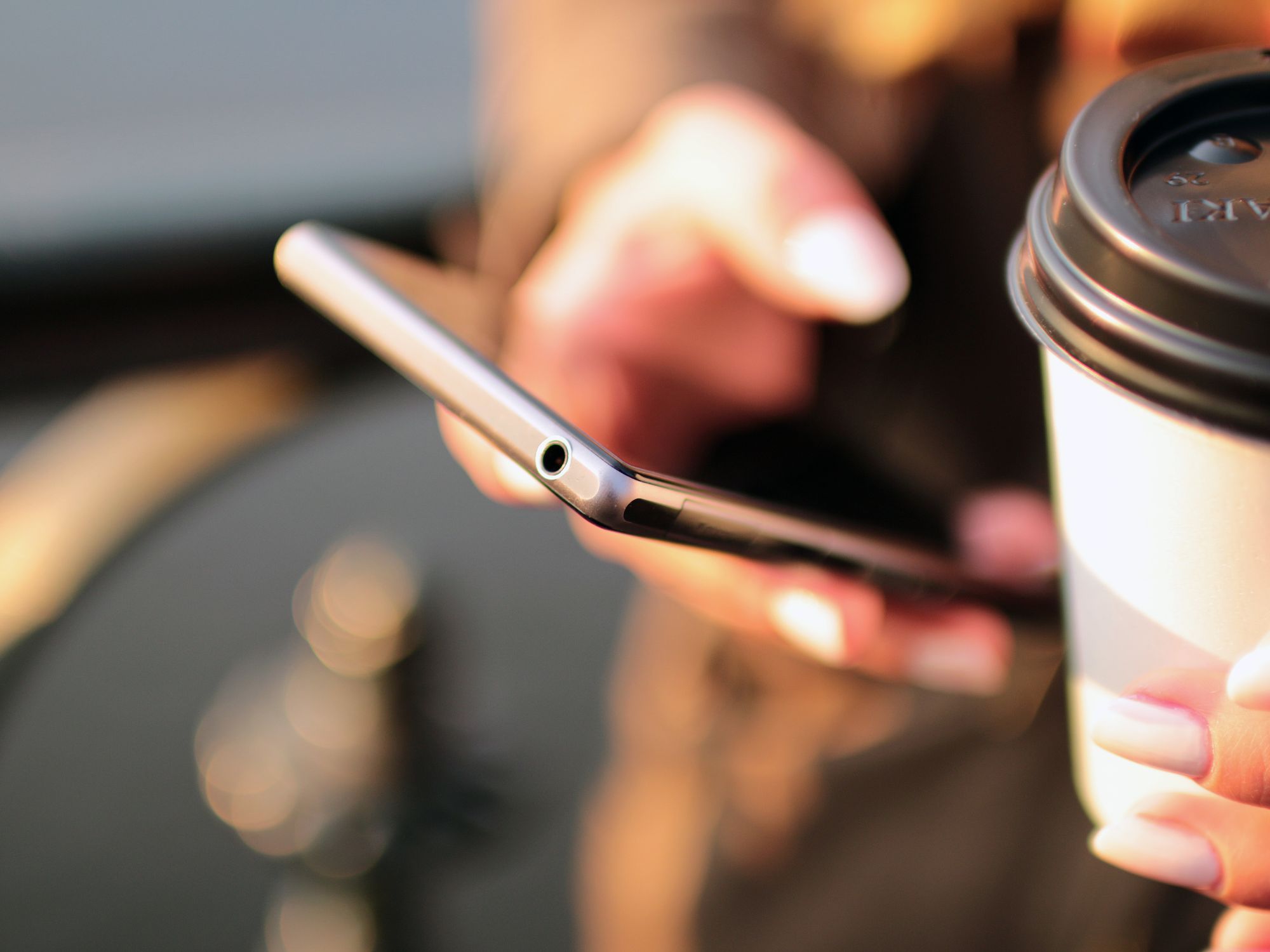 Close-up of a person holding a smartphone and a disposable coffee cup with a lid.