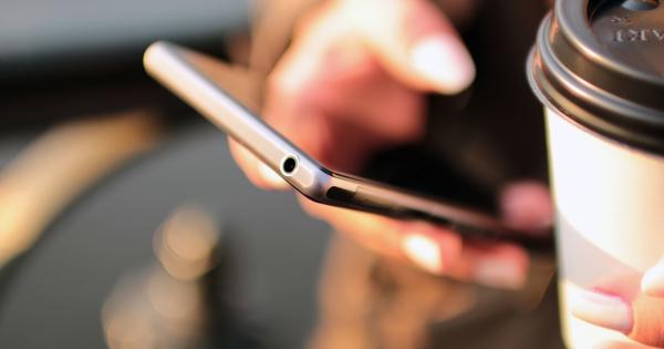 Close-up of a person holding a smartphone and a disposable coffee cup with a lid.