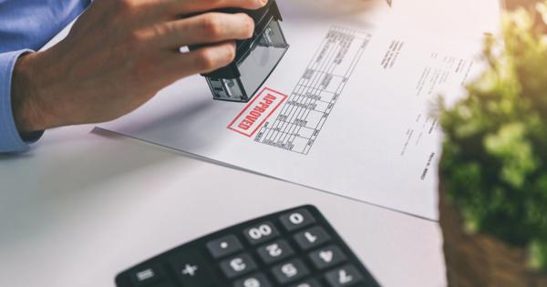 A person stamps a document marked 'APPROVED' beside a calculator and a potted plant, suggesting formal approval of a report or procurement paperwork.