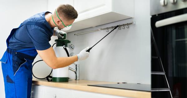 Person in protective gear spraying pesticide under kitchen cabinets.