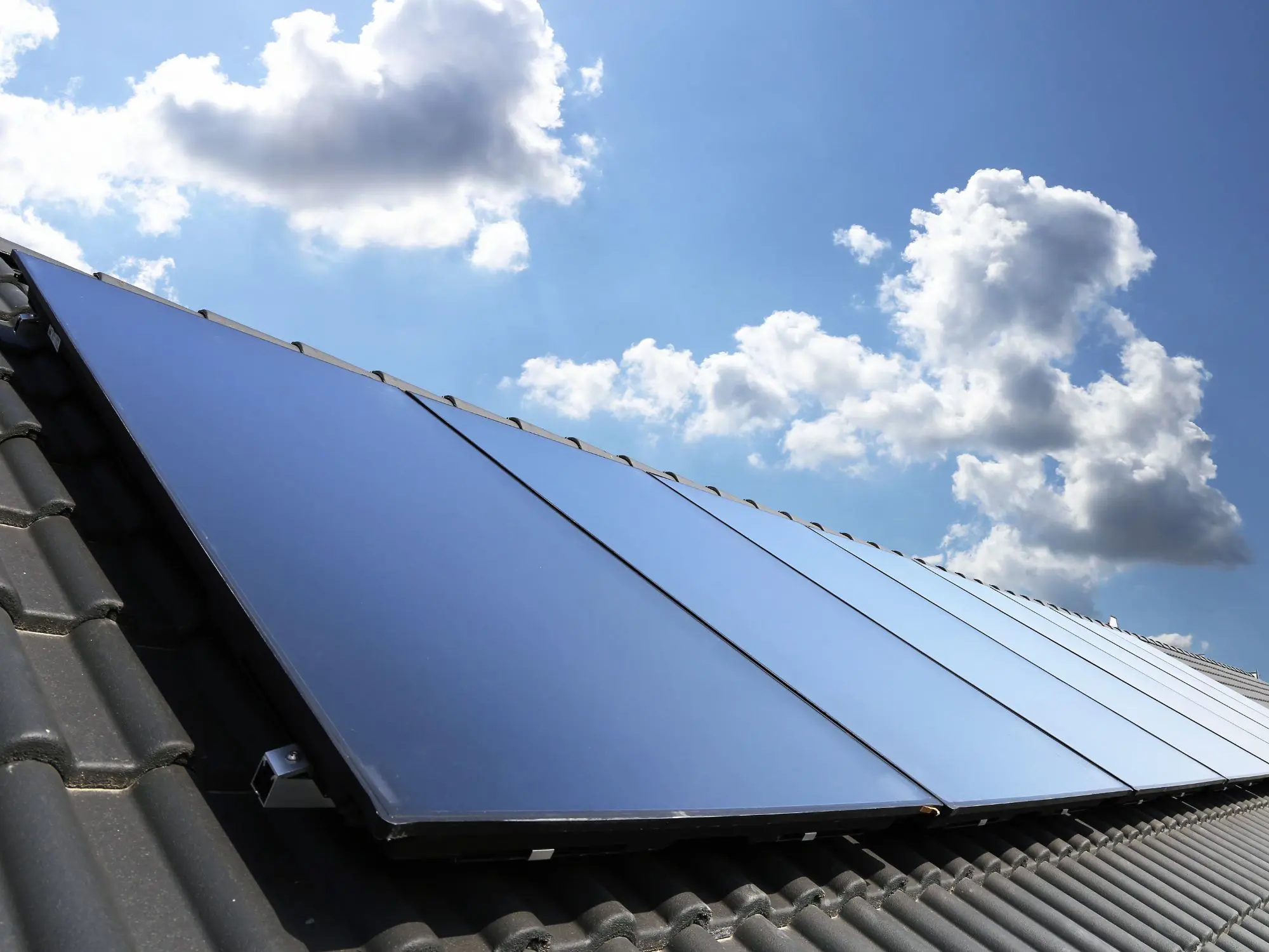 Solar panels installed on a tiled rooftop under a partly cloudy sky, reflecting sunlight.